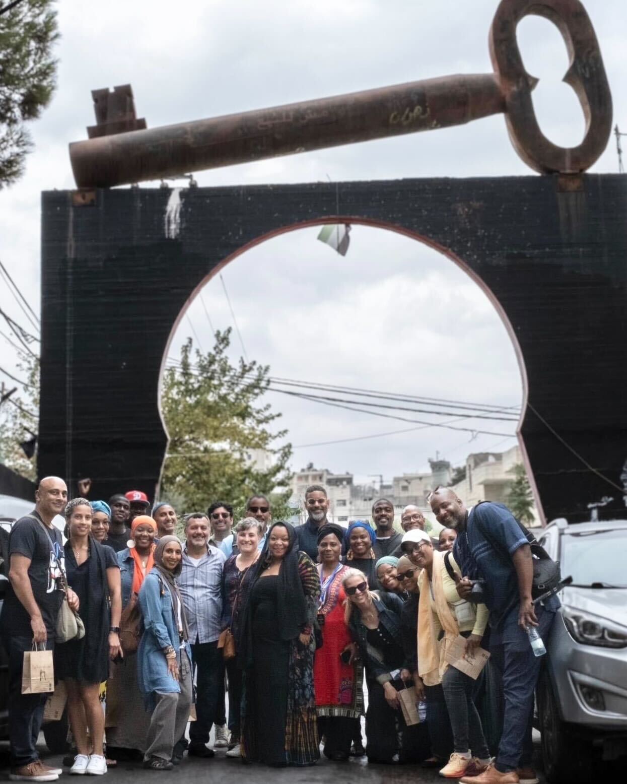 A photo of the entire Black Jerusalem travel group in front of a large iron “key of return” that rests over the entrance gate to Aida refugee camp north of Bethlehem in the central West Bank