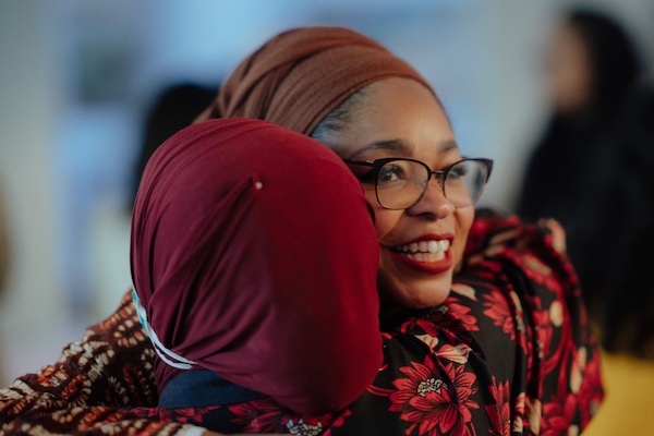 A photo of MuslimARC co-founder and executive director Margari Hill, smiling toward the camera as she hugs Pillars Senior Manager Maryam Abdul-Kareem