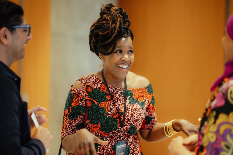 A photo of Pillars Board Member Saleemah Abdul-Ghafur, wearing a colorful floral dress and smiling to the side